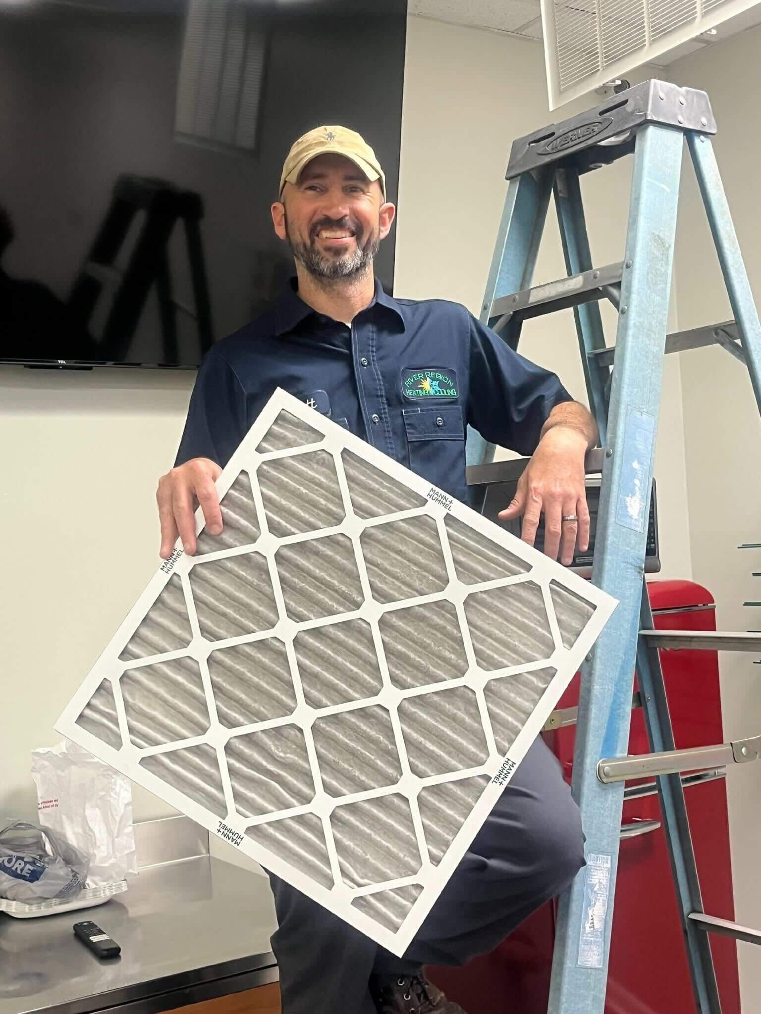 A smiling River Region technician demonstrating air filters in Millbrook
